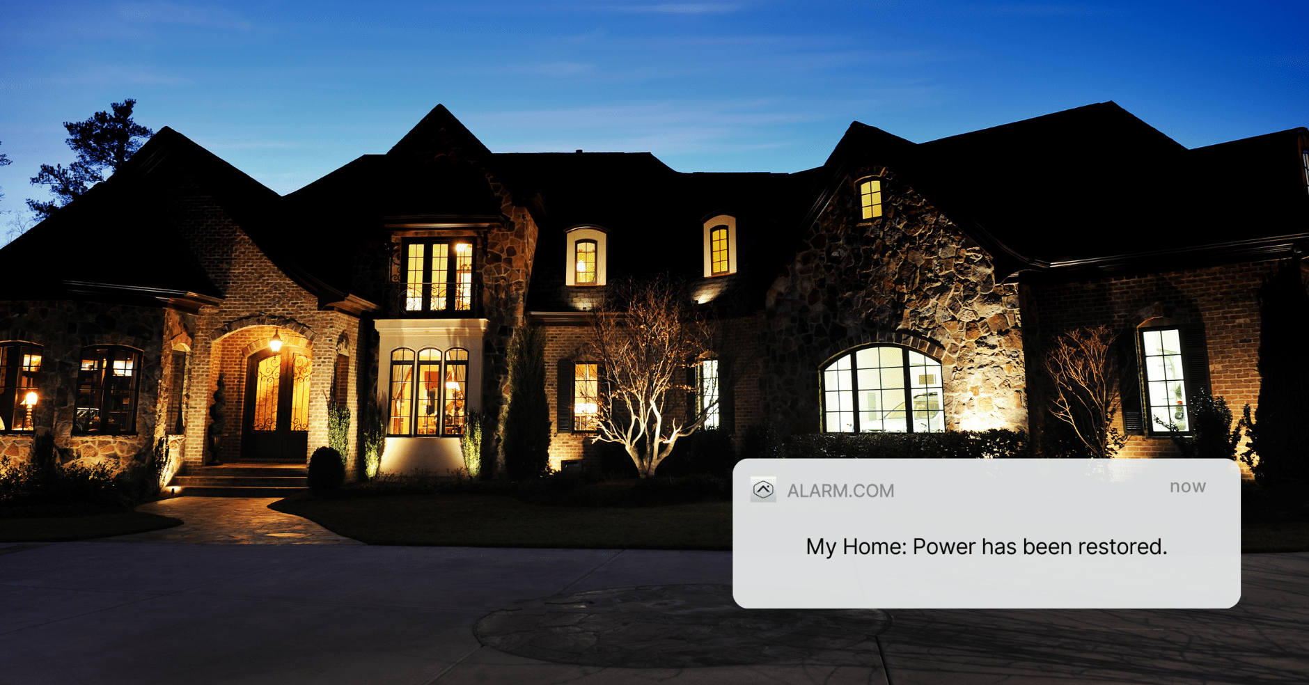 Beautiful home illuminated at dusk with a notification from Alarm.com displaying 'Power has been restored,' symbolizing home security system updates during power outages.
